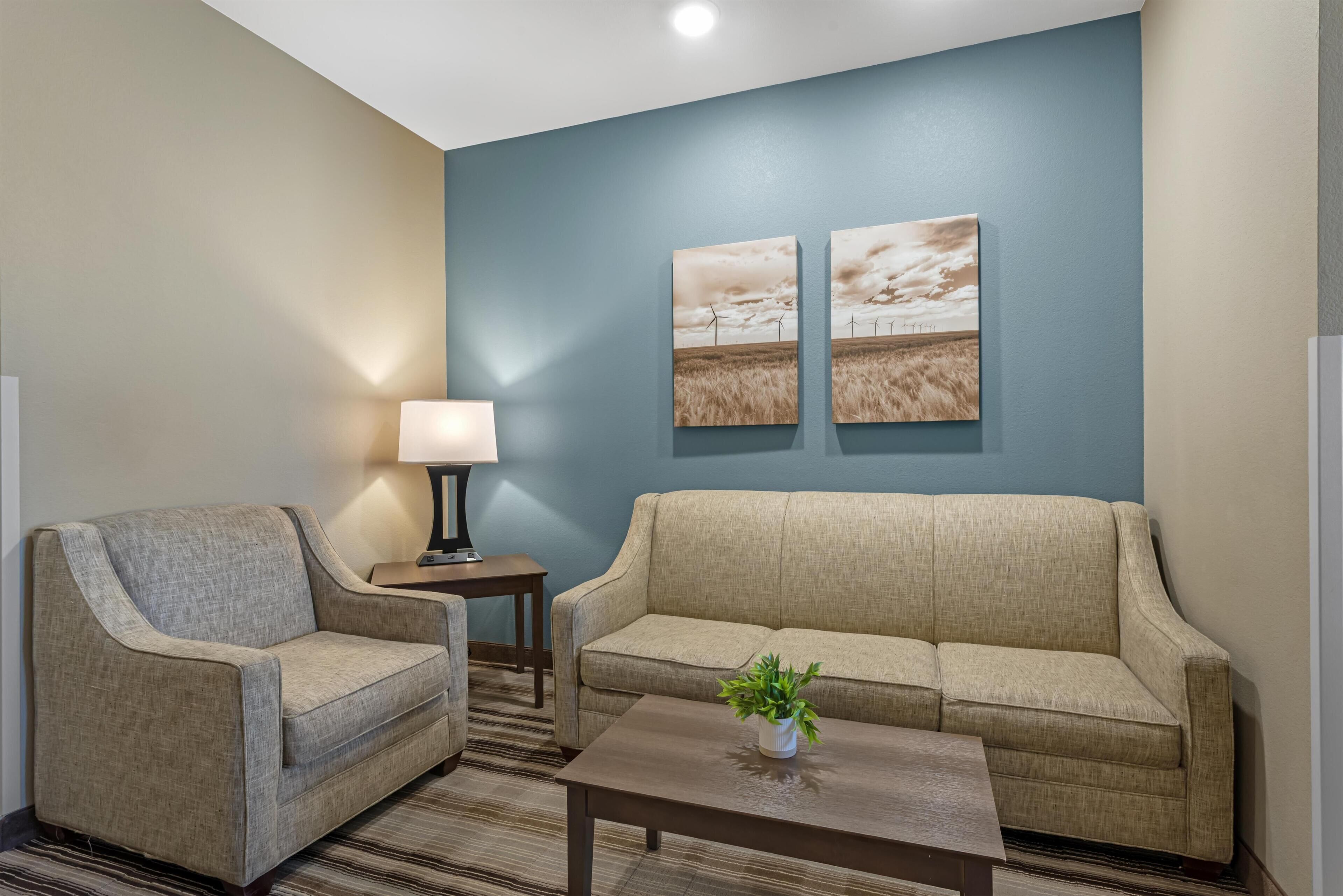 A room with a sofa, armchair, small table, lamp, and two wall-mounted paintings.
