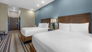 Une chambre d’hôtel avec deux lits, un banc, une table de chevet avec une lampe et une porte donnant sur un couloir.
