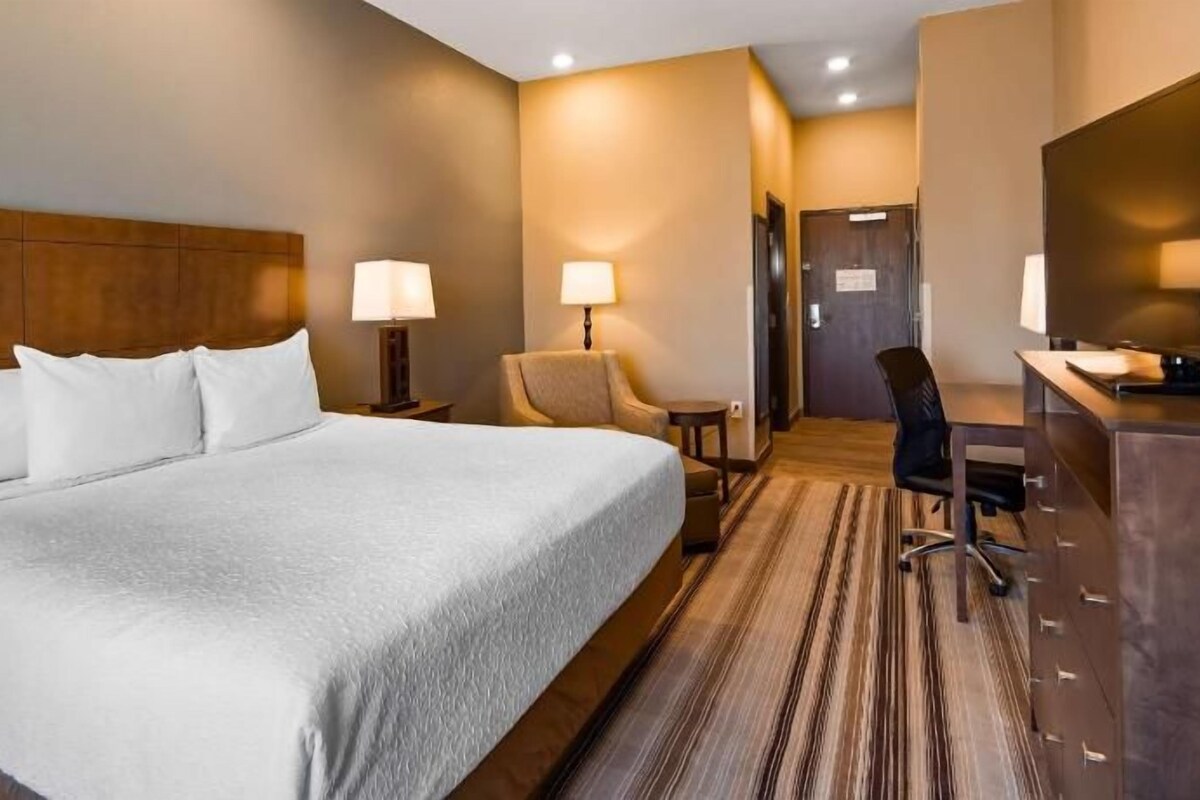A hotel room with a large bed, a desk, a chair, a lamp, and a mirror.