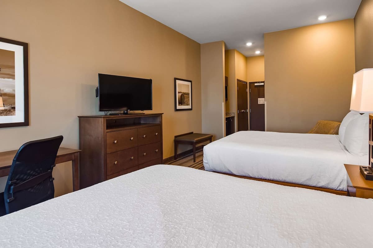 Une chambre d’hôtel avec deux lits, un bureau avec une télévision, une commode et une lampe.