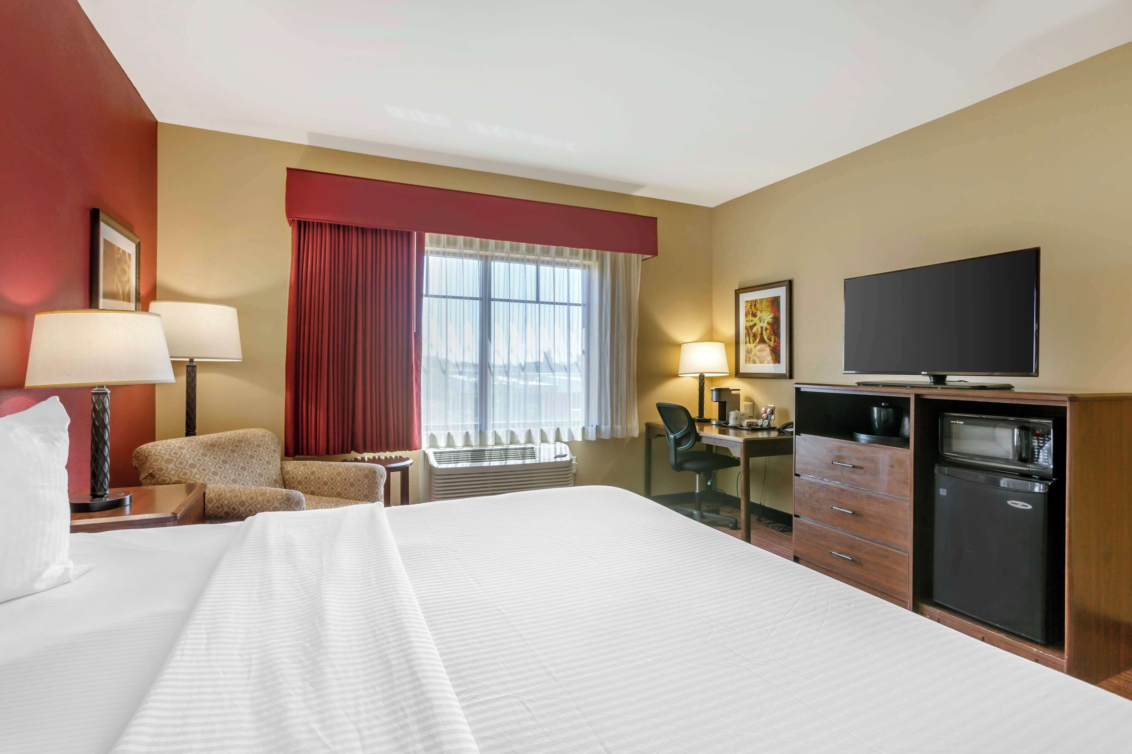 Une chambre d’hôtel avec un grand lit, un bureau avec une chaise, une télévision, un four à micro-ondes et une fenêtre avec des rideaux.