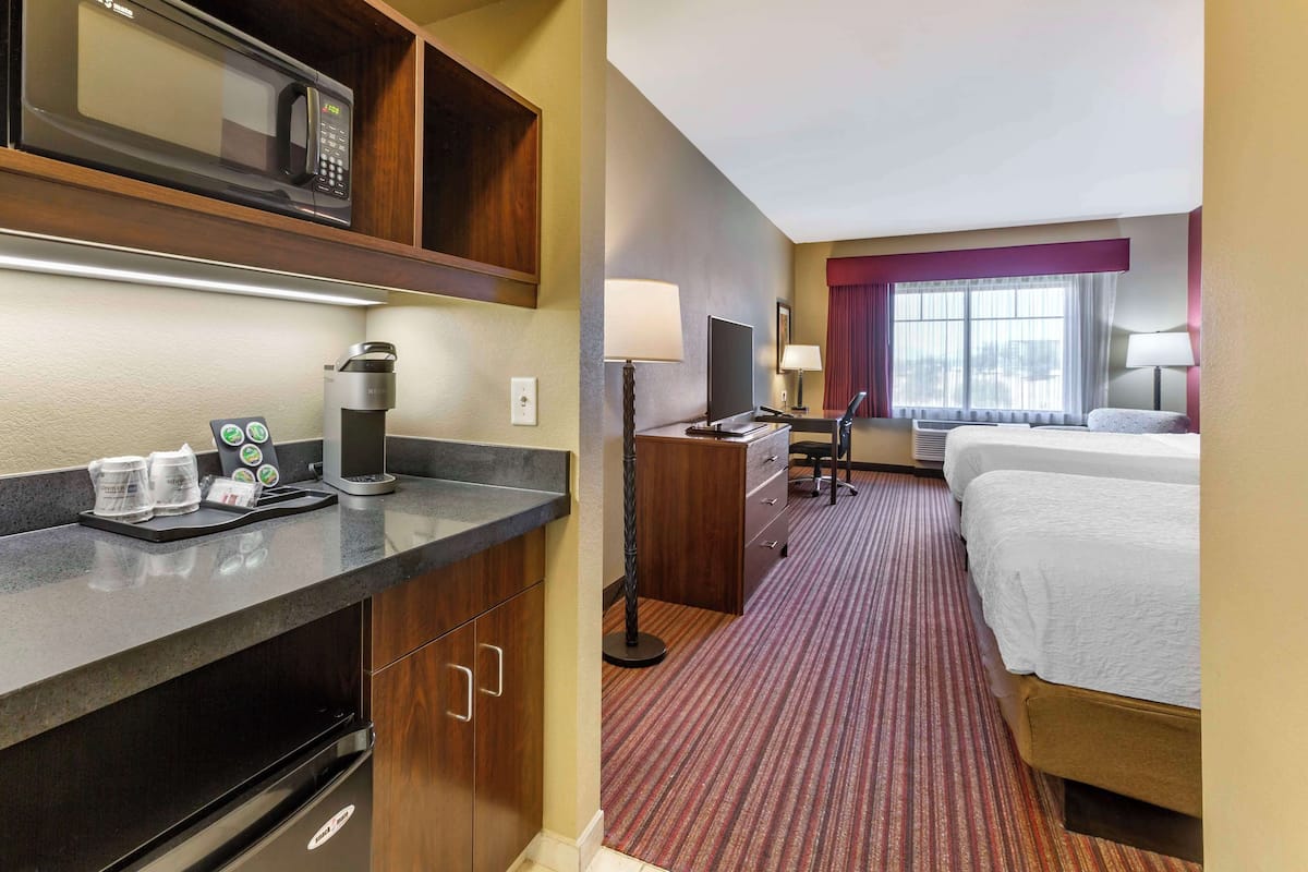 A hotel room with a bed, a desk with a computer, a microwave, a coffee maker, and a TV.