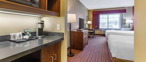 A hotel room with a bed, a desk with a computer, a microwave, a coffee maker, and a TV.