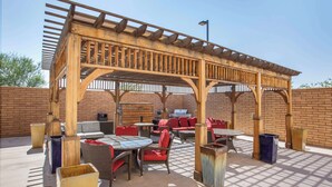 Een terras buiten met een houten pergola, zitplaatsen en een barbecuehoek.