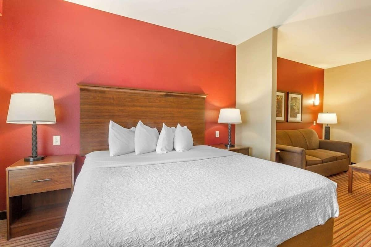 A hotel room with a large bed, two bedside tables with lamps, a wooden headboard, and a sofa in the corner.