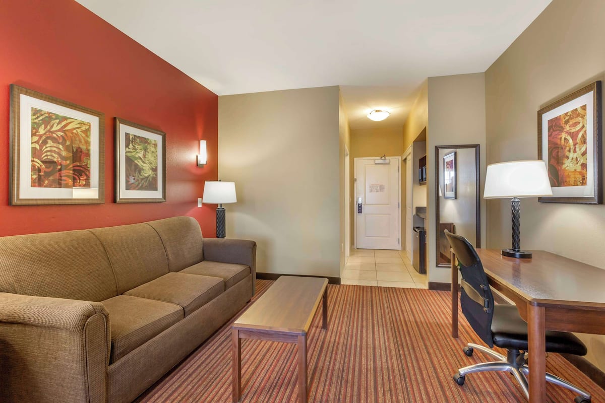 A hotel room with a sofa, a desk, and two lamps. There are framed pictures on the walls.