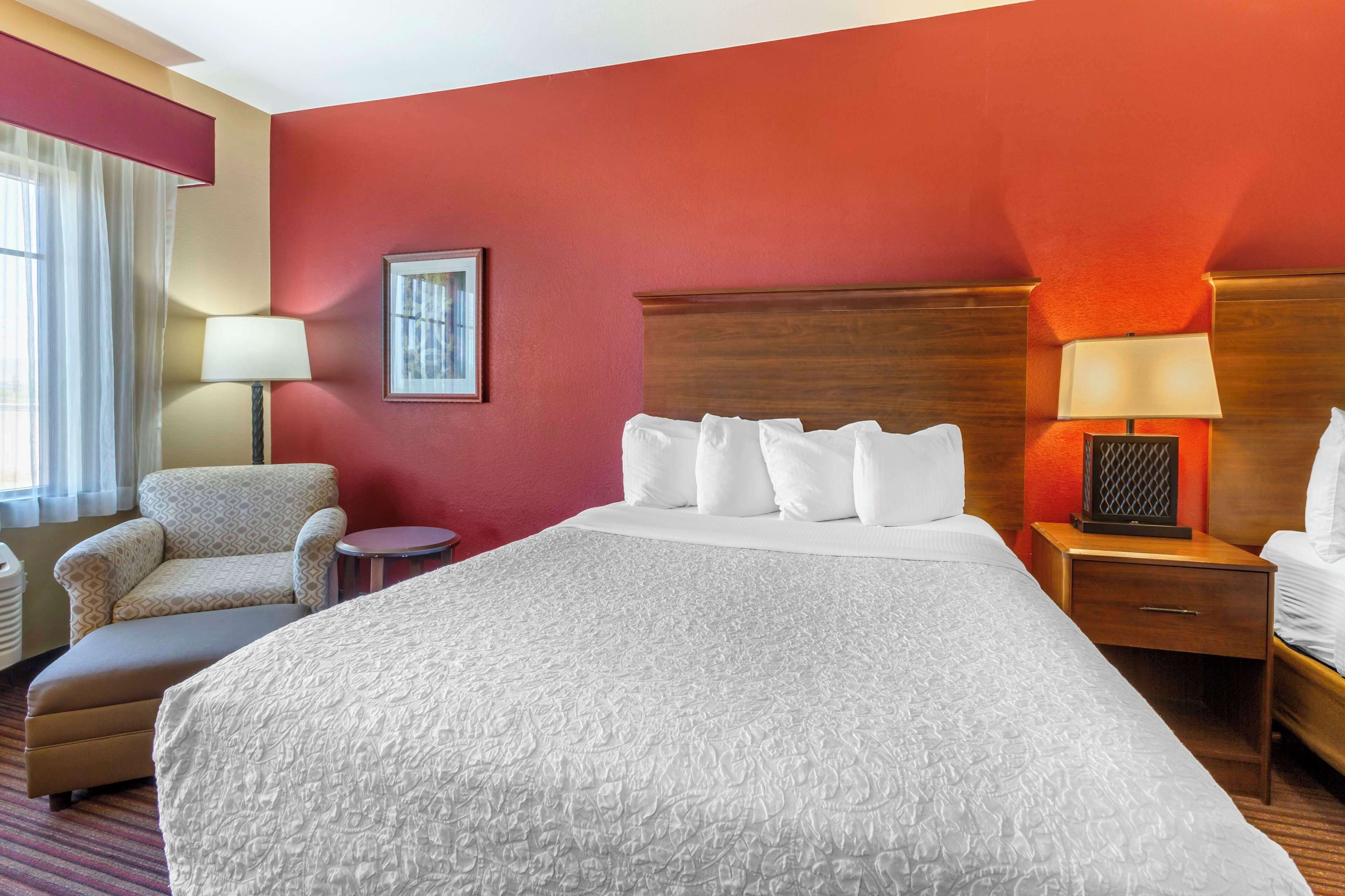 A hotel room with a large bed, a chair, a nightstand, and a lamp.
