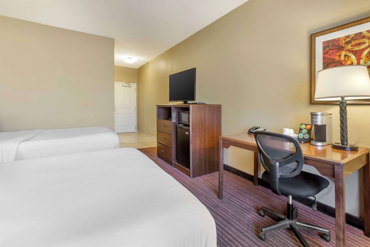 A hotel room with two beds, a desk with a computer, a chair, a lamp, and a television.