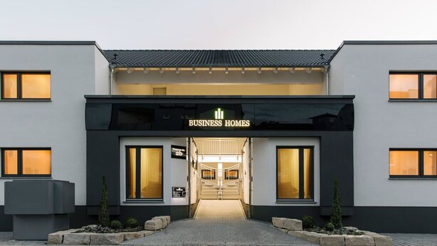 Un edificio moderno con un letrero que dice "BUSINESS HOMES" y una entrada bien iluminada.