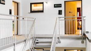 Un interior de varios niveles con una escalera central, barandillas metálicas y puertas que dan a distintas habitaciones.