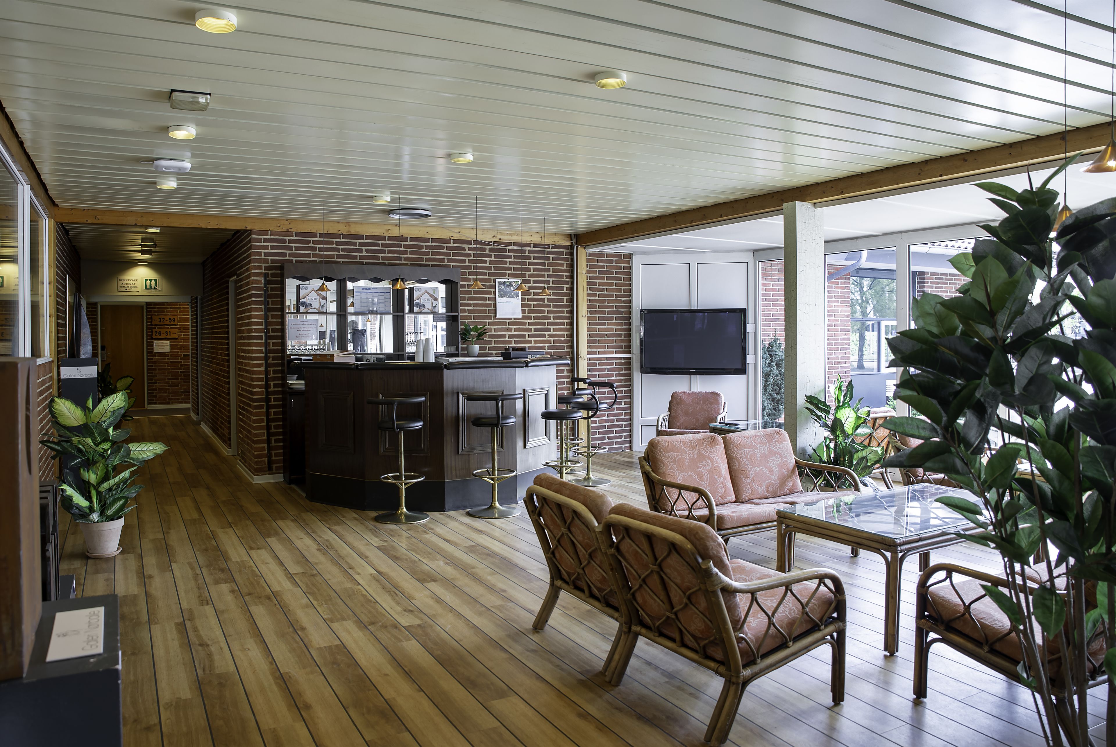 Amplio espacio interior con piso de madera, mobiliario de mimbre, una zona de bar y grandes ventanales que permiten la entrada de luz natural.