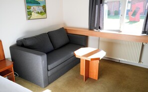 A grey sofa, a small wooden table, and a window with curtains.