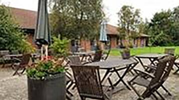 An outdoor patio area with tables and chairs, surrounded by potted plants and umbrellas.