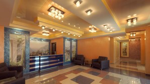 A lobby with a reception desk, seating area, and a check-in counter. - Hotel Almira (Samara)