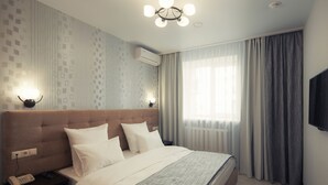 A hotel room with a large bed, bedside lamps, a phone, and a TV on the wall. - Hotel Almira (Samara)
