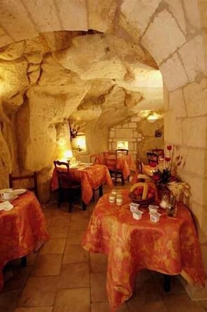 Un comedor con mesas dispuestas para dos, paredes de piedra y un ambiente cálido y acogedor.
