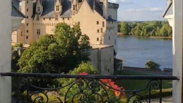 En balkong med ett smidesjärnsräcke med utsikt över ett slott som ligger vid en flod.