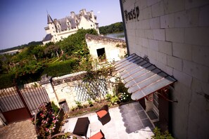 A courtyard with a castle in the background, a small garden, and a building with a metal roof. - Hôtel le Bussy (Montsoreau)