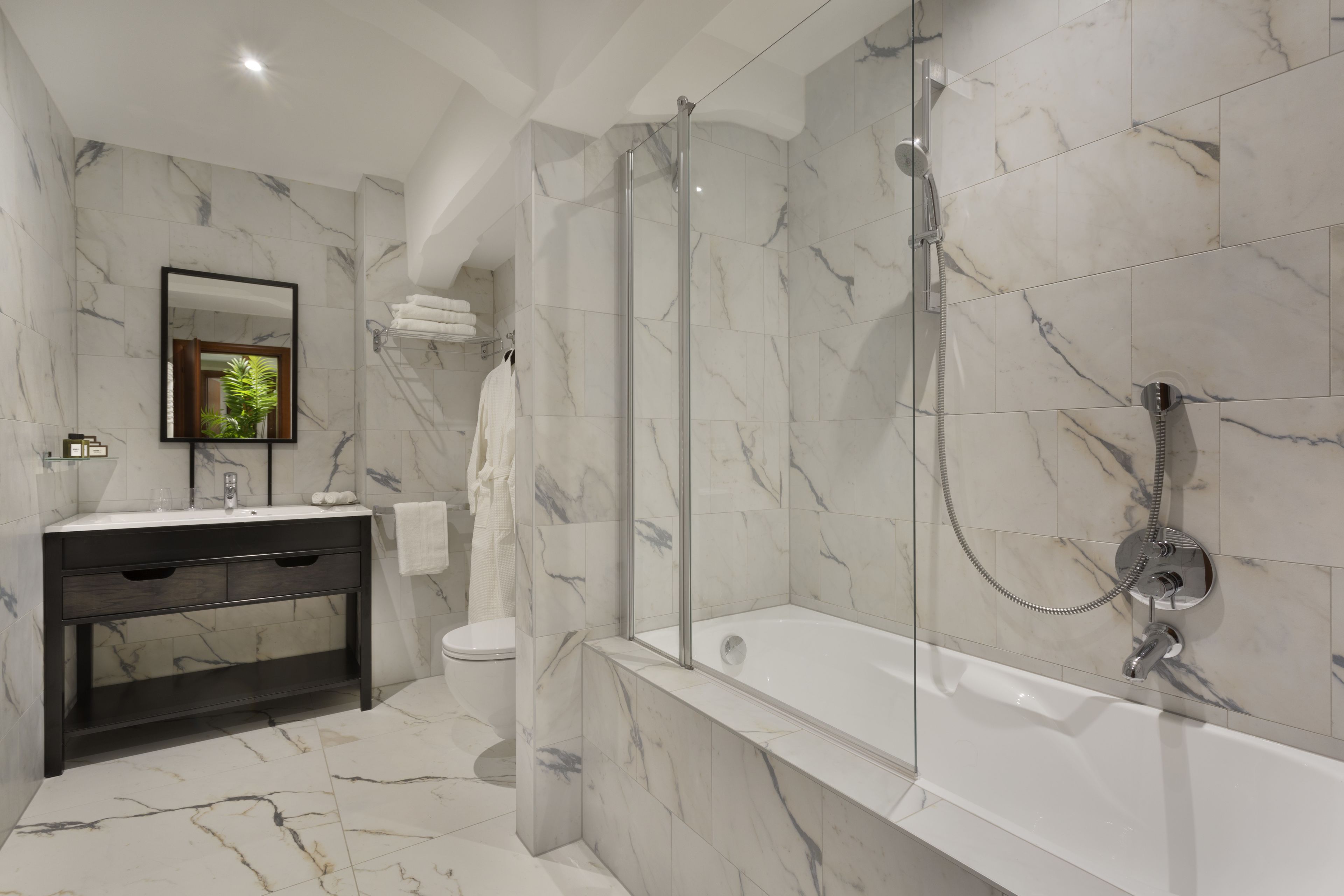 Un baño moderno con ducha envuelta en vidrio, una bañera blanca y un mueble de tocador de madera oscura.