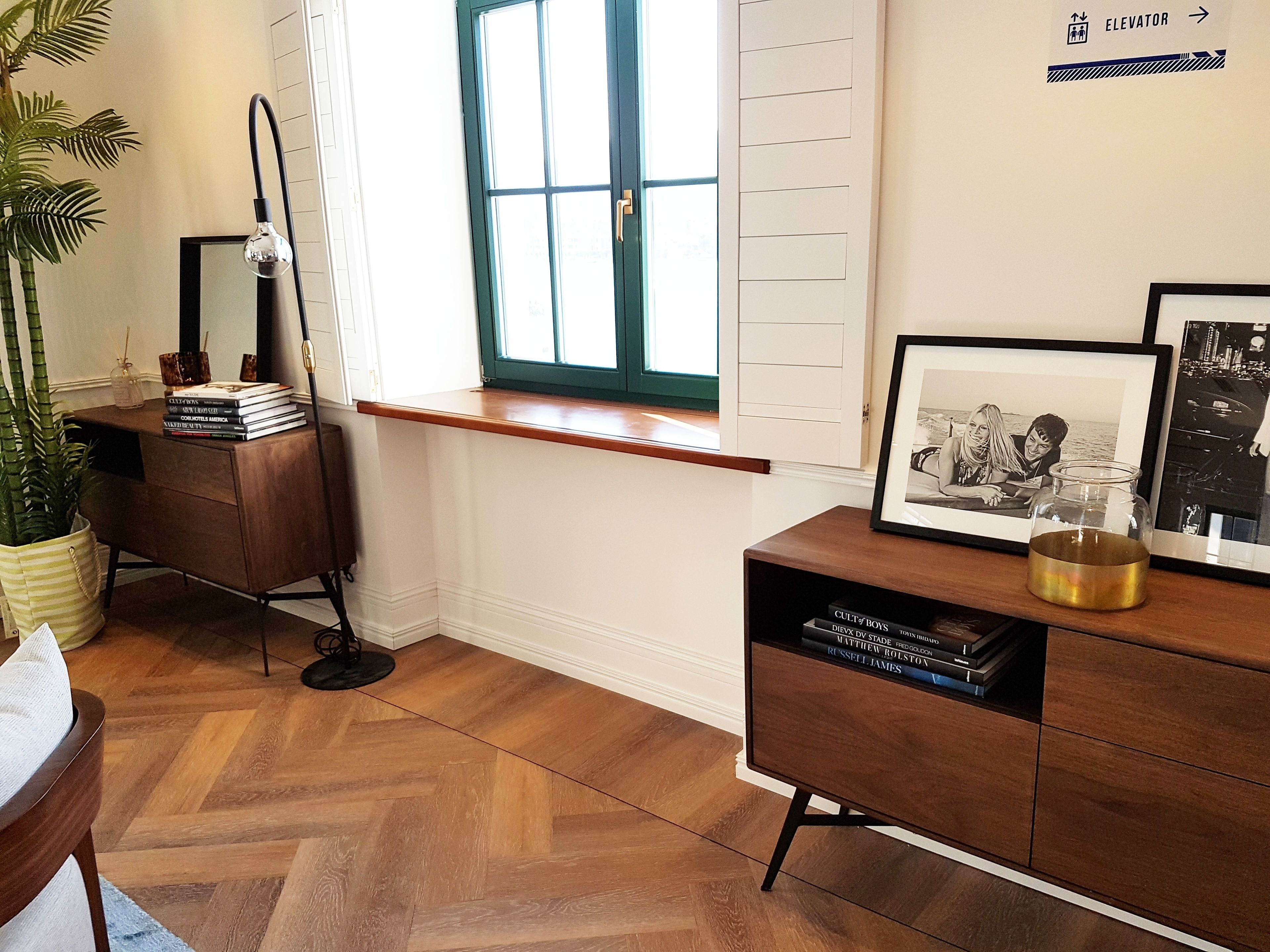 Una stanza con pavimento in parquet a spina di pesce, una scrivania con specchio, una finestra con persiane e una libreria piena di libri.