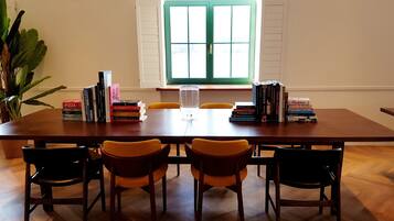 Una mesa de comedor con libros, un vaso y sillas en una habitación con ventana y una planta.