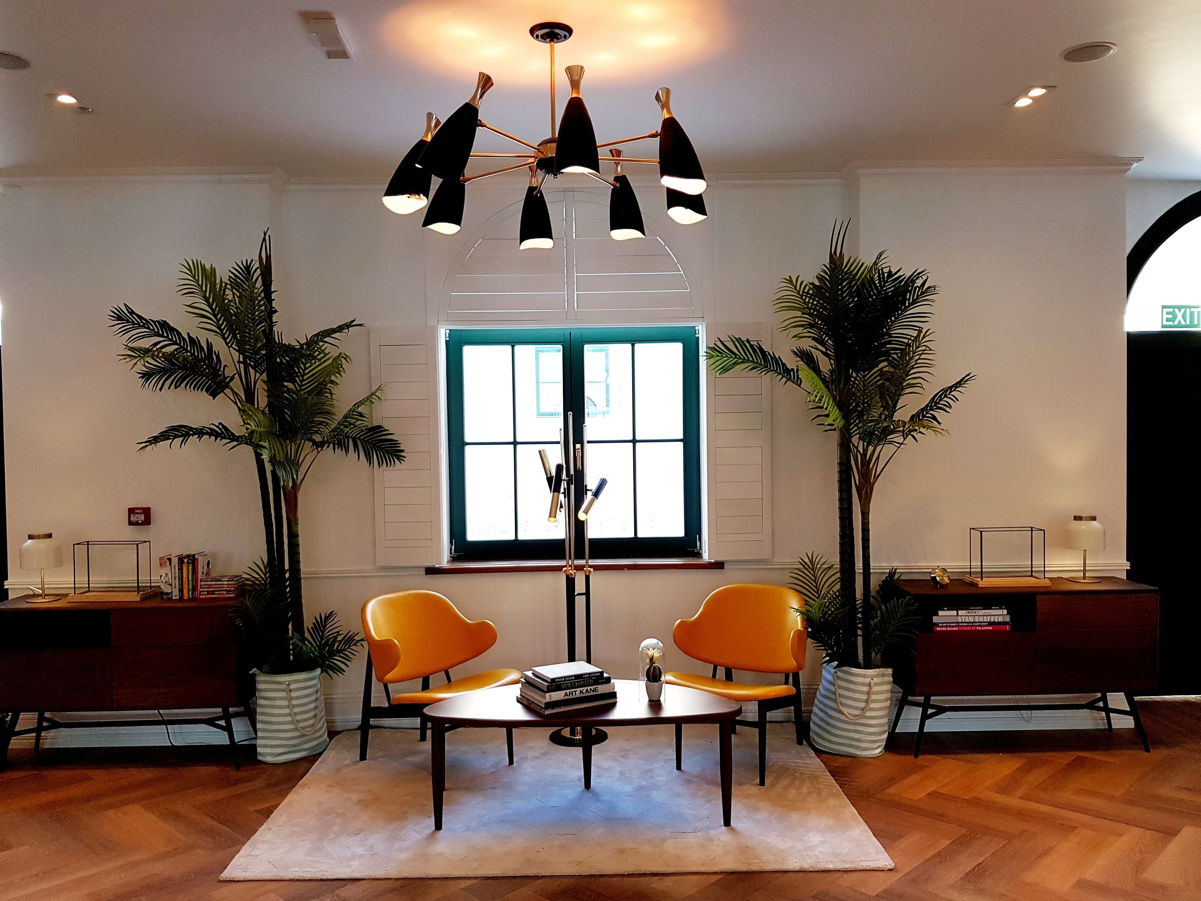 Un hall d’entrée moderne avec une table centrale, deux fauteuils orange, un lustre et de grandes fenêtres.