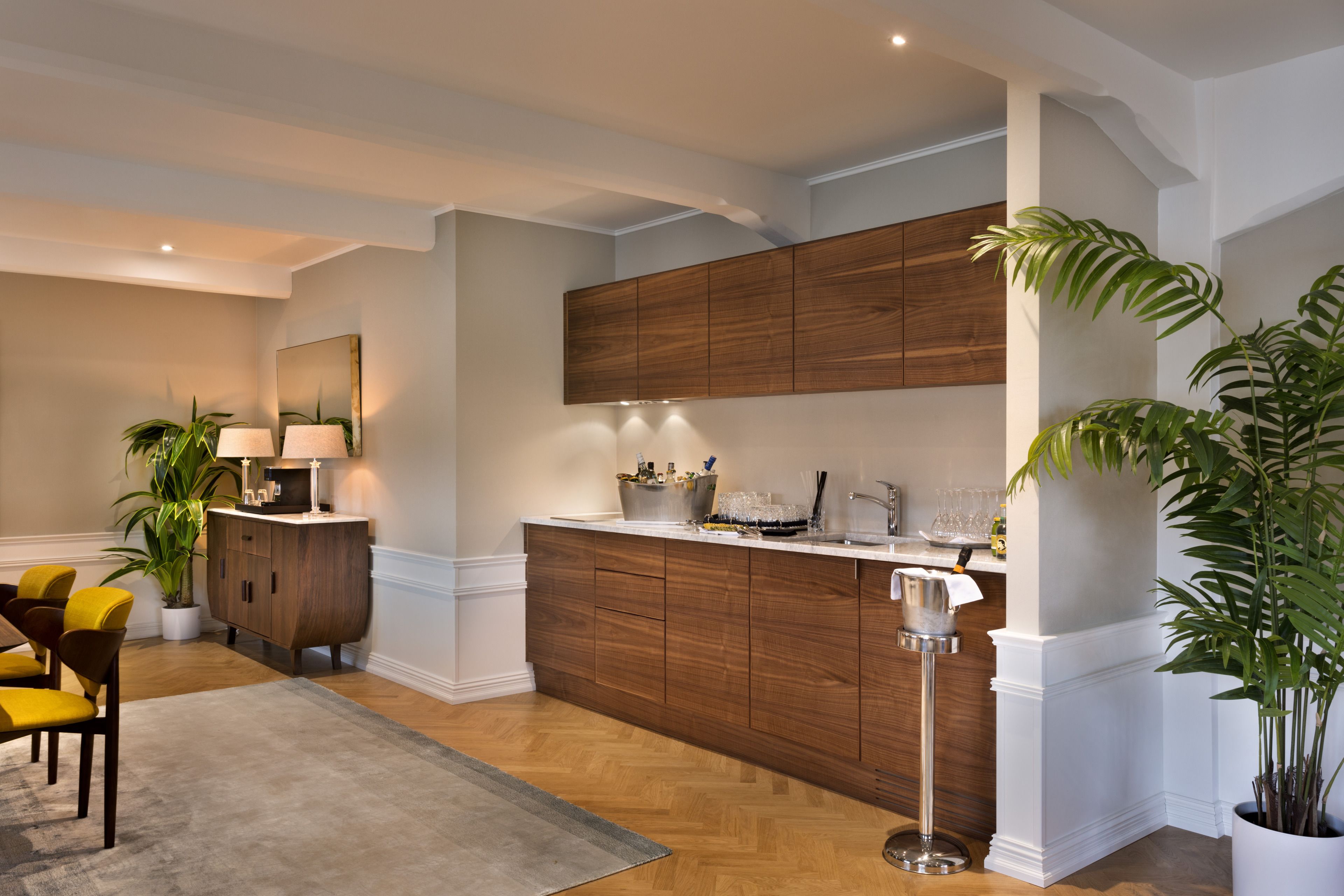 Una cocina moderna con armarios de madera, encimera blanca y zona de comedor con sillas amarillas.