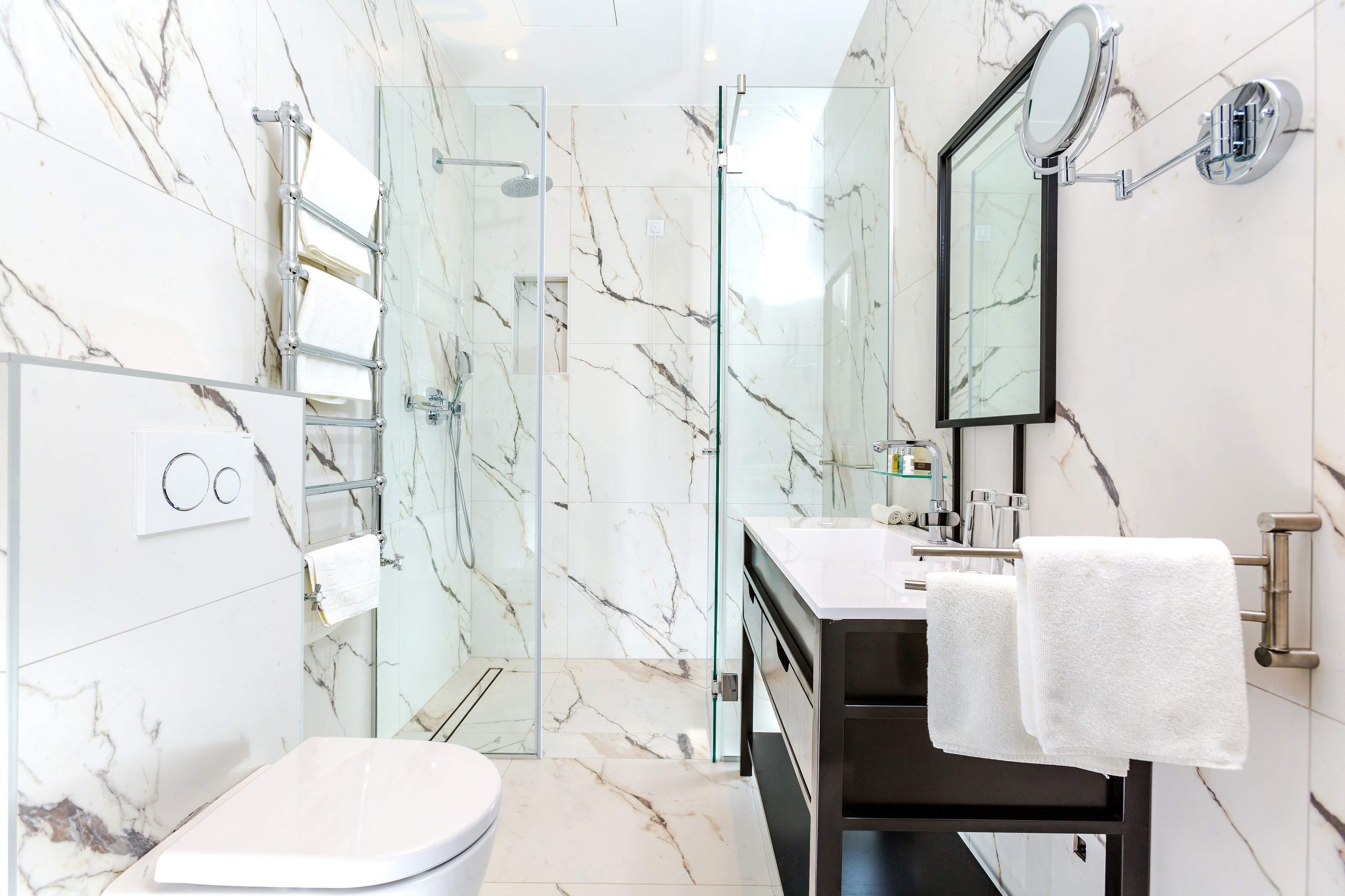 A modern bathroom with a glass-enclosed shower, a white toilet, and a vanity with a mirror and towel rack.