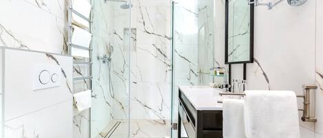 A modern bathroom with a glass-enclosed shower, a white toilet, and a vanity with a mirror and towel rack.