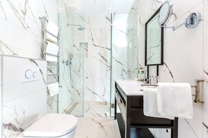 Un baño moderno con ducha de vidrio, inodoro blanco y tocador con espejo y toallero.