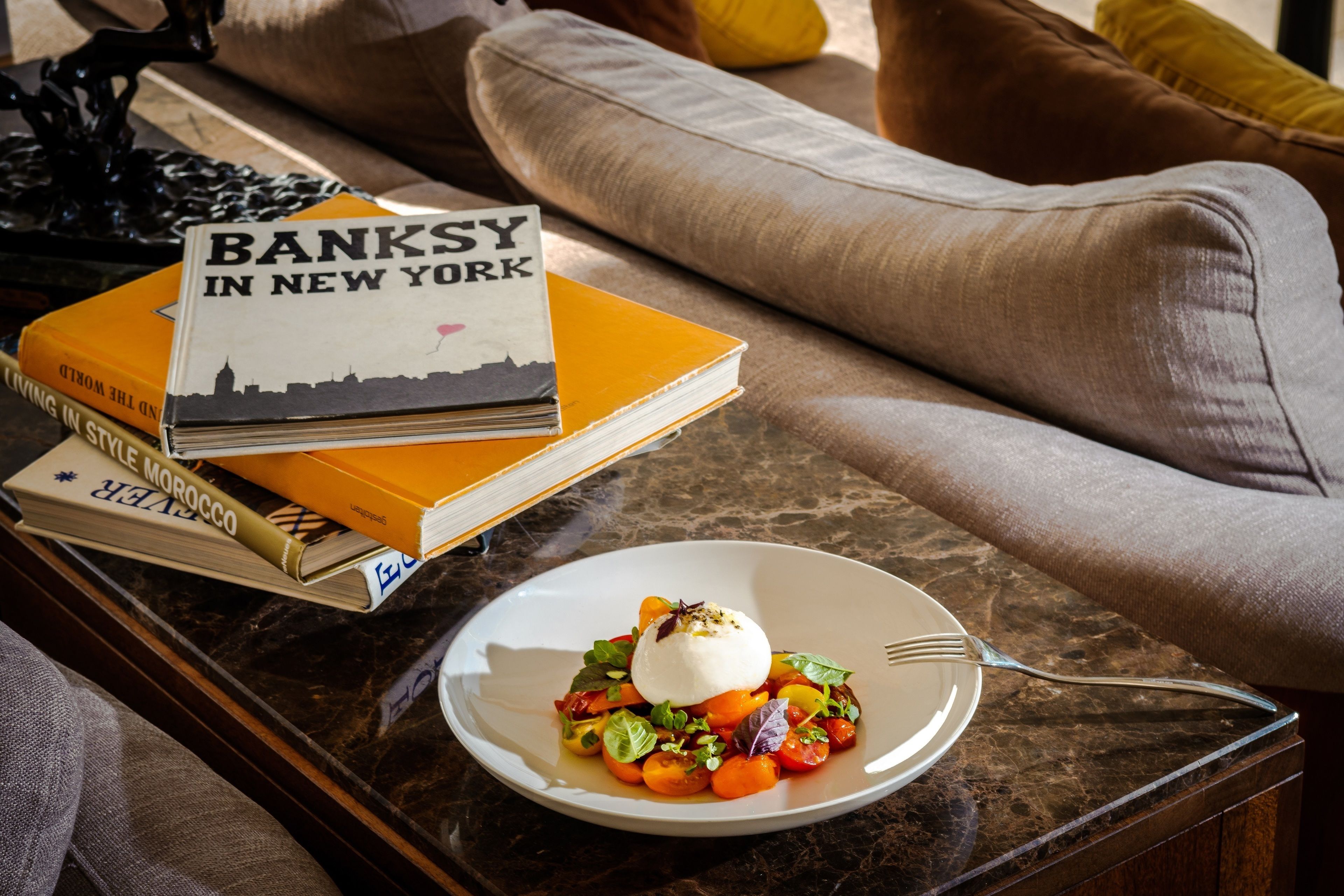 Una mesa de comedor con un plato de comida, un tenedor y una pila de libros.