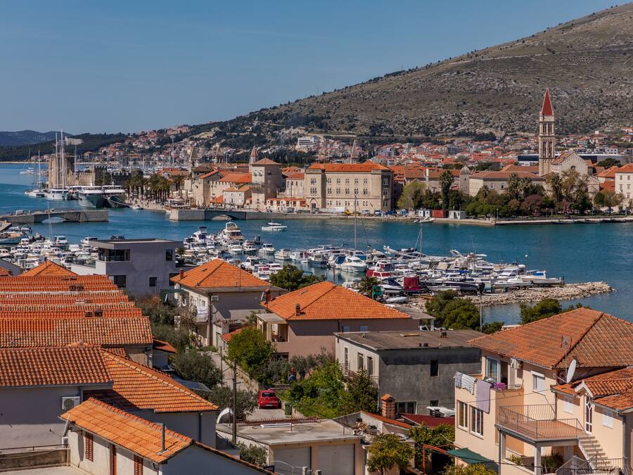 Un pueblo costero con un puerto deportivo, edificios de techo rojo y una colina al fondo.