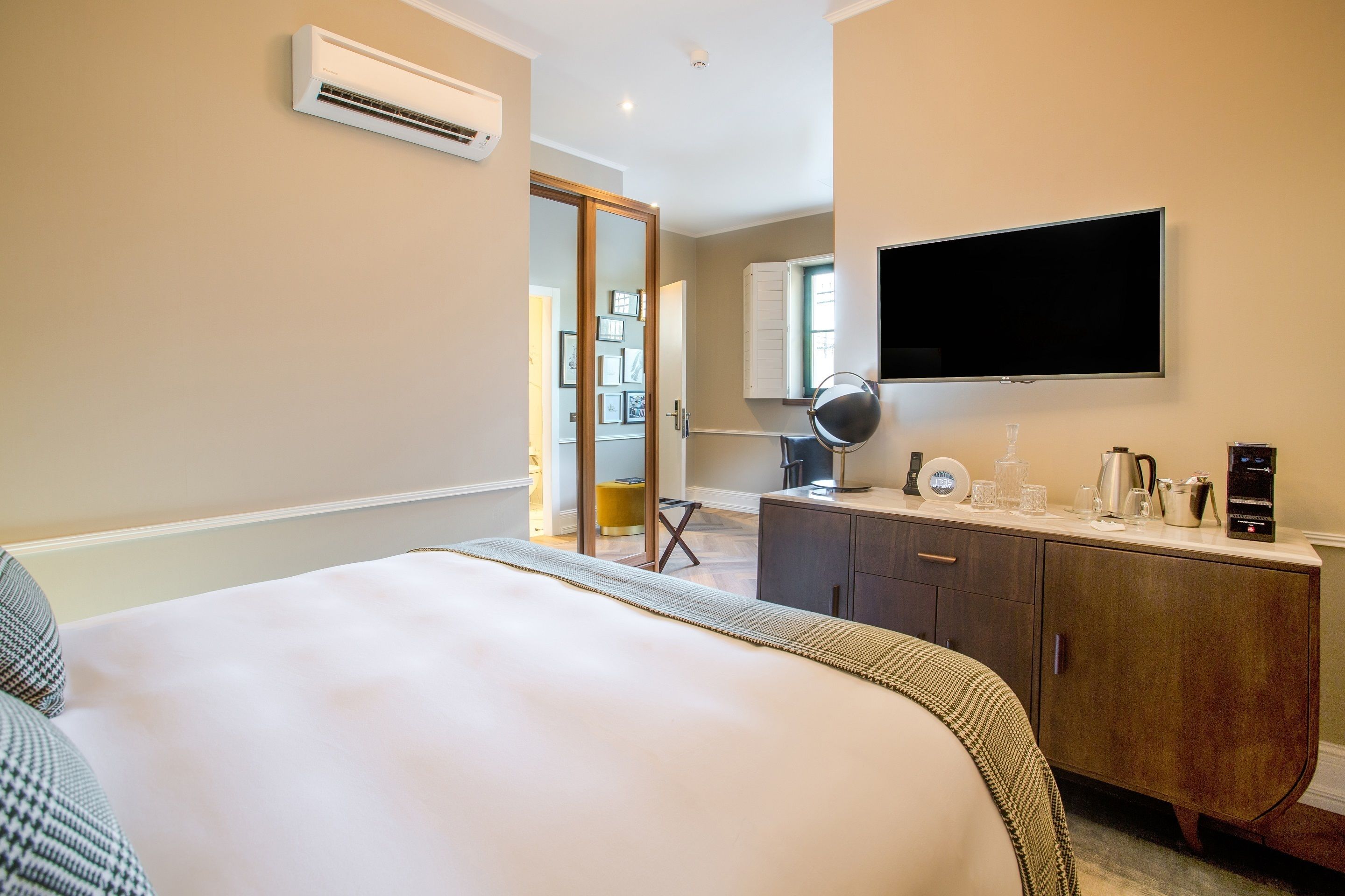 Una habitación de hotel con una cama, un televisor montado en la pared, una cafetera y una mesita con una lámpara y tazas.