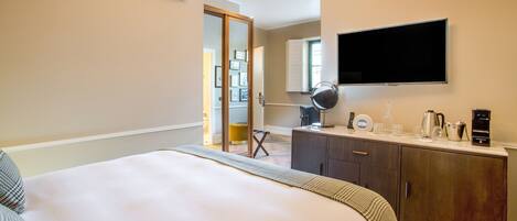 Una habitación de hotel con una cama, un televisor montado en la pared, una cafetera y una mesita con una lámpara y tazas.