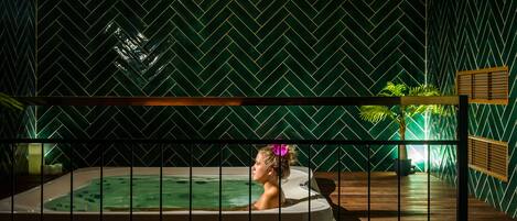 A spa area with a hot tub, wooden deck, and a green herringbone-patterned wall.