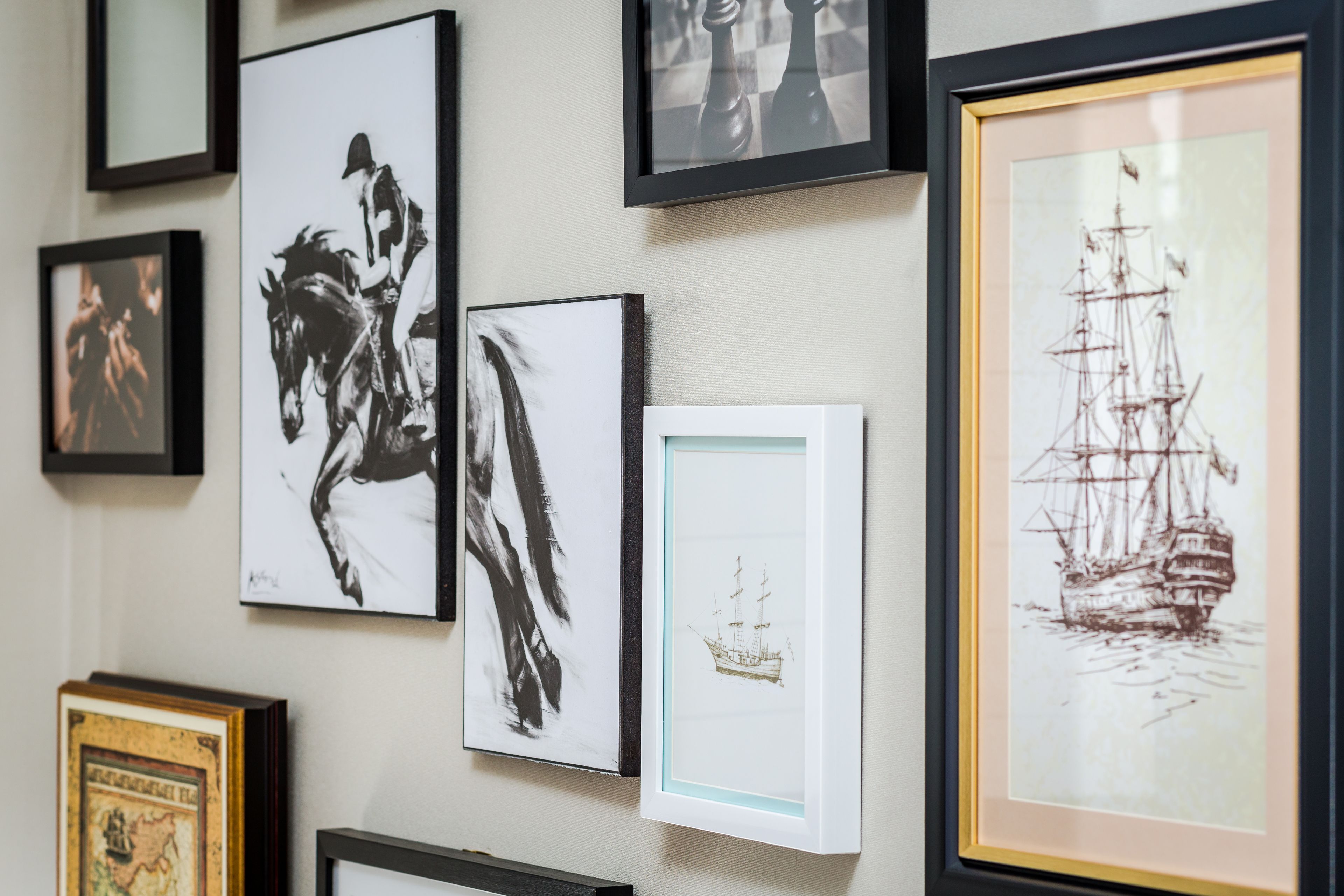 Un mur orné de divers tableaux encadrés, dont un représentant un cheval, une œuvre d’art abstrait et un navire.