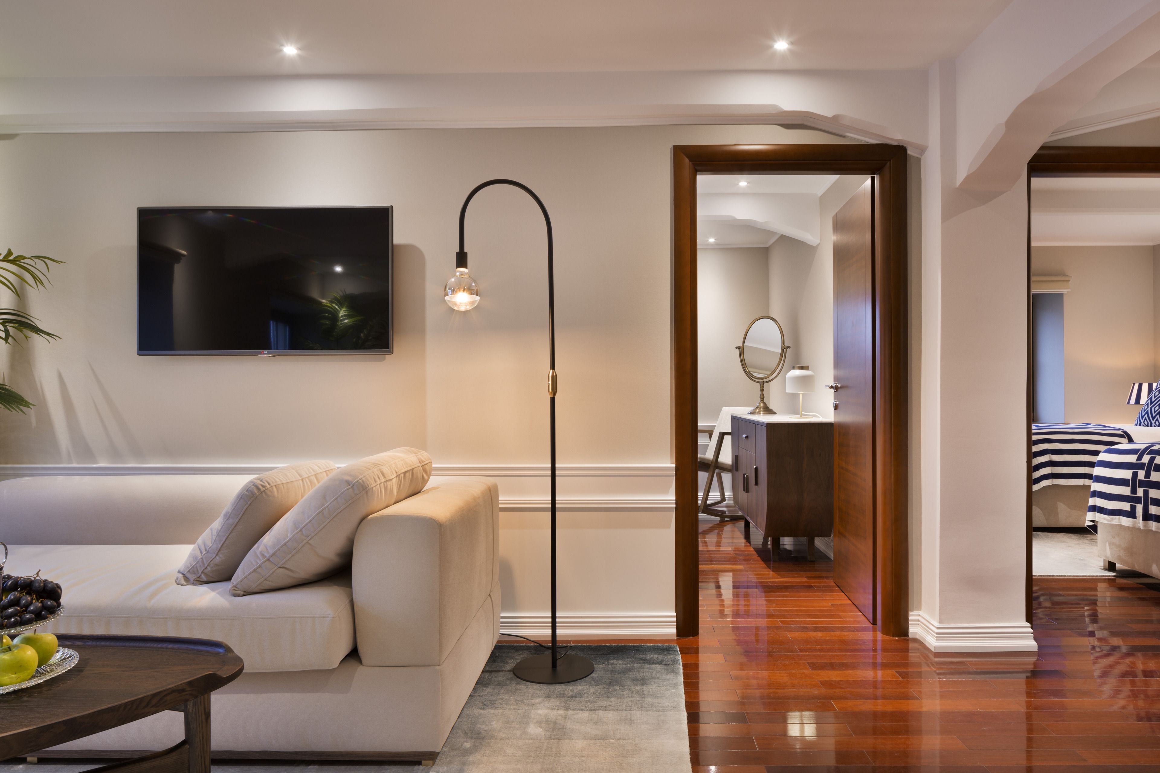 A modern living room with a sofa, a floor lamp, and a flat-screen TV mounted on the wall.