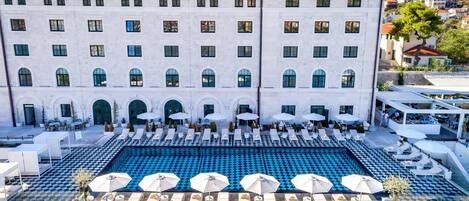 Un edificio grande con un área de piscina que incluye tumbonas y sombrillas.
