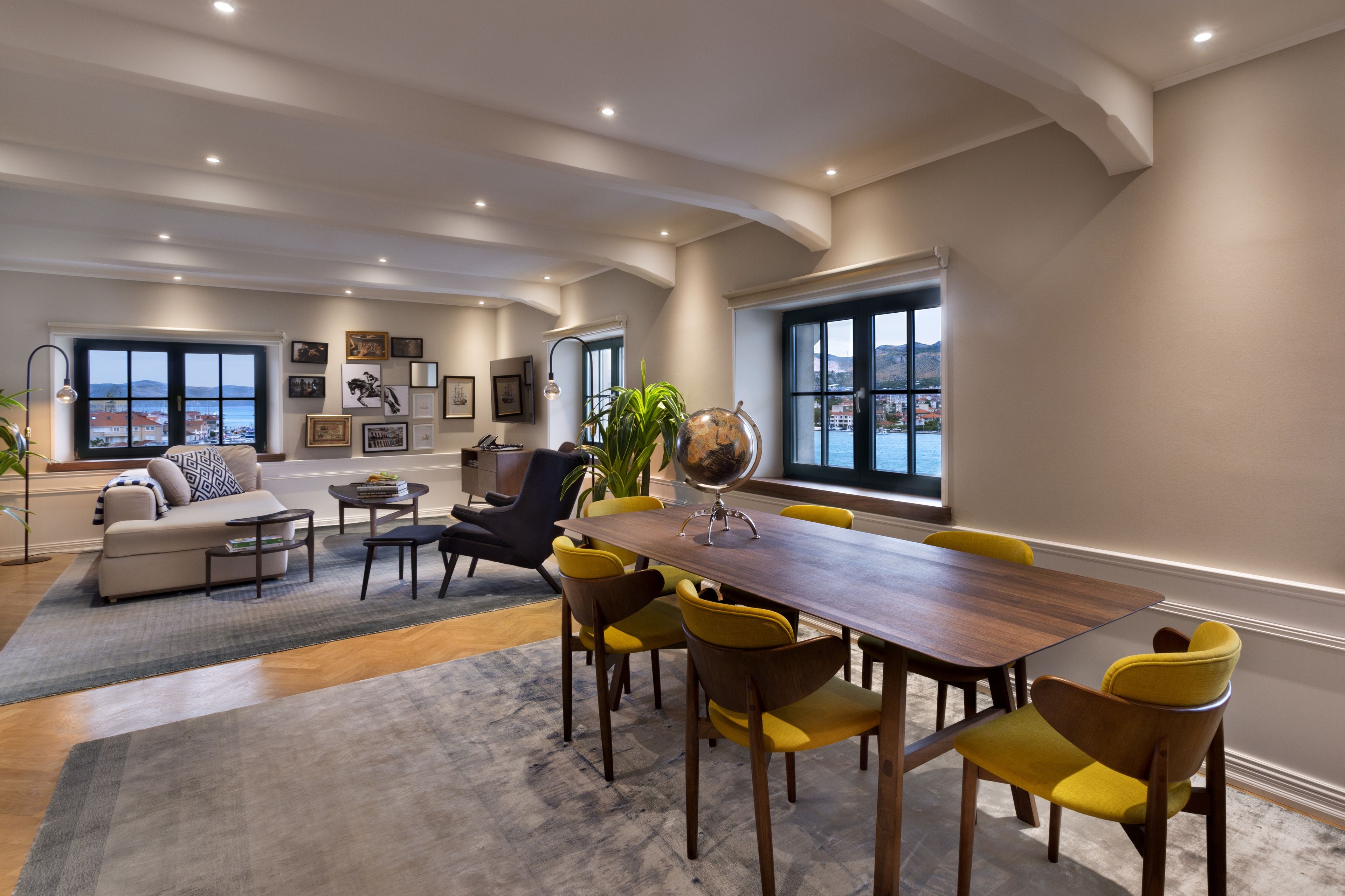 A modern living room with a wooden dining table, yellow chairs, a sofa, and a large window with a view.