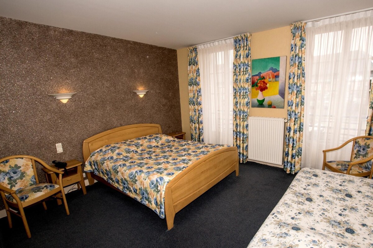 Een hotelkamer met een houten bed, twee stoelen, een schilderij en een radiator.