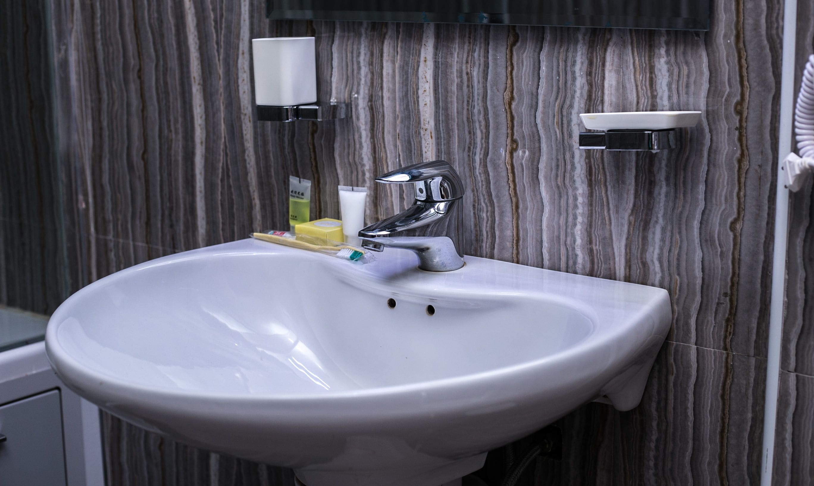 A bathroom with a white sink, chrome faucet, and marble-patterned walls.