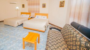 A hotel room with two single beds, a sofa, a wooden table, and a patterned armchair. - Erata Hotel (Accra)