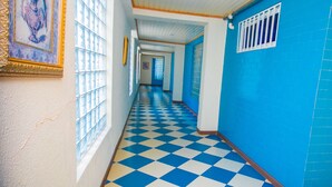 A hallway with a blue and white checkered floor, a blue wall, and a window with a decorative frame. - Erata Hotel (Accra)