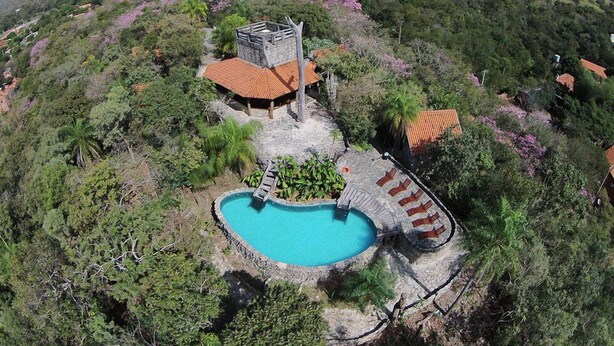 Ein Pool, umgeben von Steinmauern, ein kleines Gebäude mit rotem Dach und üppiges Grün an einem Hang.
