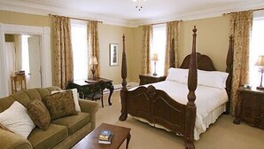A traditional bedroom with a four-poster bed, a wooden coffee table, a sofa, and a ceiling fan. - DesBarres Manor Inn (Guysborough)