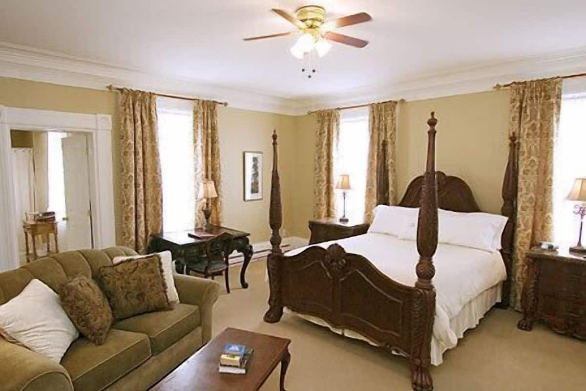 Un dormitorio tradicional con una cama con dosel, una mesita de madera, un sofá y un ventilador de techo.