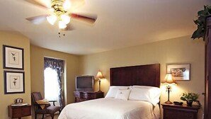 A bedroom with a large bed, a ceiling fan, a television on a nightstand, and framed pictures on the wall.