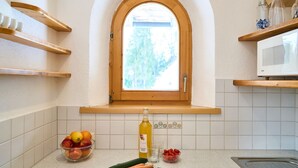 A kitchen with a window, wooden shelves, a bowl of fruit, a bottle of olive oil, and a microwave. - Das Habitat (Leutasch)