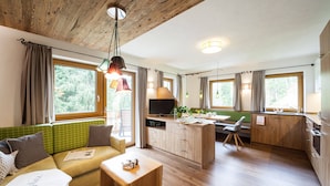 A cozy room with a sofa, a small table, a TV, and a kitchenette. - Das Habitat (Leutasch)