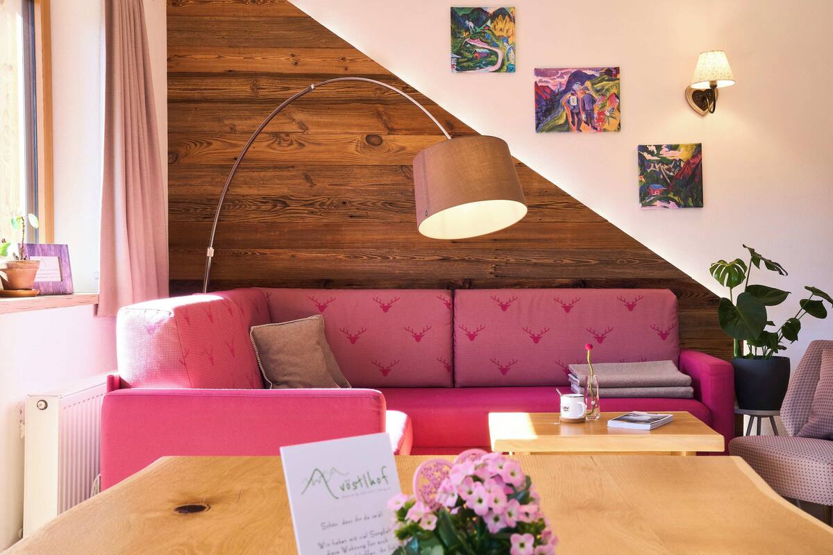 A cozy room with a pink sofa, a wooden ceiling, and a table with a vase of flowers.